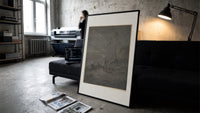 Two robed figures under starry sky print in a slim black frame leaning on a dark sofa in a concrete print studio