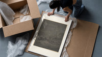 Two robed figures under starry sky framed print being unpacked from protective bubble wrap and a box