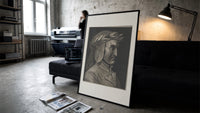 Man wearing laurel wreath in profile print in a slim black frame leaning on a dark sofa in a concrete print studio
