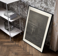 Two robed figures on cliff at night poster in a black frame leaning beside a shelf in a raw-plaster loft