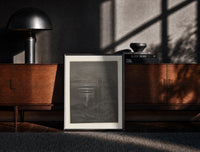Black-framed Two robed figures on cliff at night print on a moody console with designer coffee-table books
