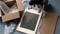 Two robed figures on cliff at night framed print being unpacked from protective bubble wrap and a box
