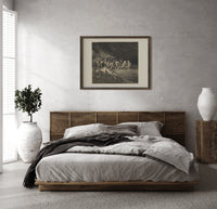 Charon ferrying damned souls print in a dark wood frame above a rattan bed on a plaster wall