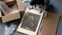 Winged demons flying above two robed figures framed print being unpacked from protective bubble wrap and a box