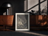 Black-framed Two figures facing a winged monster print on a moody console with designer coffee-table books