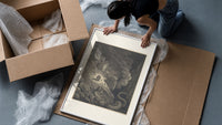 Two figures facing a winged monster framed print being unpacked from protective bubble wrap and a box