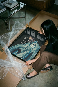 Woman unboxing a Drake If You're Reading This print and display frame from a box with bubble wrap