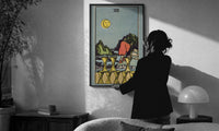 Eight of Cups print in a slim black frame being hung on a sunlit wall in a monochrome room
