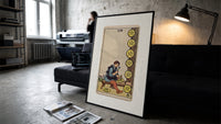 Craftsman carving pentacle coins print in a slim black frame leaning on a dark sofa in a concrete print studio