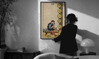 Eight of Pentacles print in a slim black frame being hung on a sunlit wall in a monochrome room