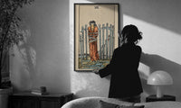 Eight of Swords print in a slim black frame being hung on a sunlit wall in a monochrome room