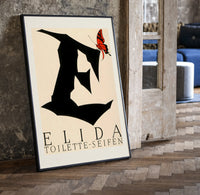 Butterfly on giant letter E print in a black frame leaning beside a vintage door on parquet