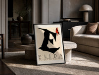Butterfly on giant letter E print in a black frame leaning on a travertine table in a sunlit lounge