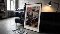 Woman on bicycle with tennis racket print in a slim black frame leaning on a dark sofa in a concrete print studio
