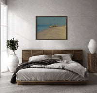 Fishermen with boat on beach print in a dark wood frame above a rattan bed on a plaster wall