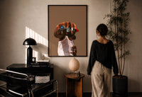 Fist with a Blue Gemstone Ring print in a black frame on a sunlit plaster wall, a woman looking on beside a mushroom lamp