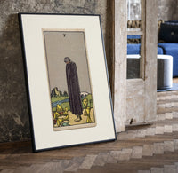 Cloaked figure among spilled cups print in a black frame leaning beside a vintage door on parquet