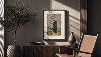 Cloaked figure among spilled cups poster framed above a fluted sideboard beside an olive tree