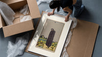 Cloaked figure among spilled cups framed print being unpacked from protective bubble wrap and a box