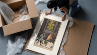 Two beggars passing lit stained-glass window framed print being unpacked from protective bubble wrap and a box