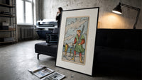 Man collecting swords by shore print in a slim black frame leaning on a dark sofa in a concrete print studio