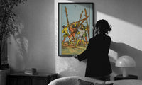 Five of Wands print in a slim black frame being hung on a sunlit wall in a monochrome room