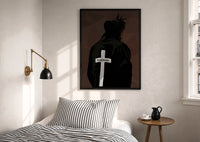 Forgiven Cross Hoodie print in a black frame above a bed with striped linens, a brass wall lamp and a sunlit window