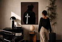 Forgiven Cross Hoodie print in a black frame on a sunlit plaster wall, a woman looking on beside a mushroom lamp