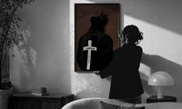 Forgiven Cross Hoodie print in a slim black frame being hung on a sunlit wall in a monochrome room