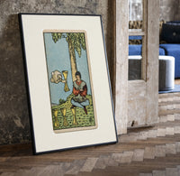 Seated man under tree with cups print in a black frame leaning beside a vintage door on parquet