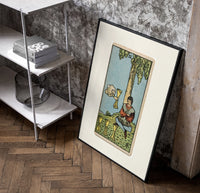 Seated man under tree with cups poster in a black frame leaning beside a shelf in a raw-plaster loft