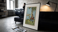 Seated man under tree with cups print in a slim black frame leaning on a dark sofa in a concrete print studio