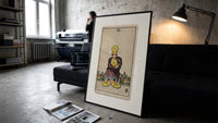 Man clutching gold pentacle coins print in a slim black frame leaning on a dark sofa in a concrete print studio