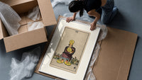 Man clutching gold pentacle coins framed print being unpacked from protective bubble wrap and a box