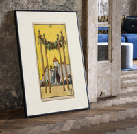Four Wands tarot card scene print in a black frame leaning beside a vintage door on parquet
