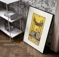 Four Wands tarot card scene poster in a black frame leaning beside a shelf in a raw-plaster loft