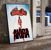 Akira red bike and rider framed anime poster on white print in a black frame leaning beside a vintage door on parquet