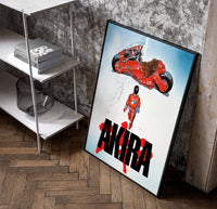 Akira red bike and rider framed anime poster on white poster in a black frame leaning beside a shelf in a raw-plaster loft