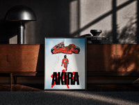 Black-framed Akira red bike and rider framed anime poster on white print on a moody console with designer coffee-table books