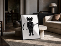 KAWS Chum figure with swoosh line framed poster on white print in a black frame leaning on a travertine table in a sunlit…