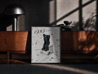 Black-framed Black KAWS Companion on Nike shoeboxes framed sketch poster print on a moody console with designer…