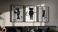 Black and white KAWS Nike framed poster set of 3 triptych in three black frames on a grey wall above a leather sofa