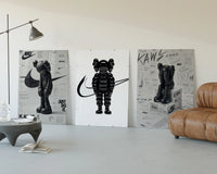 Black and white KAWS Nike framed poster set of 3 three-panel set displayed beside a brown leather sofa