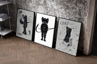 Black and white KAWS Nike framed poster set of 3 set of three black-framed prints leaning against a raw-plaster wall