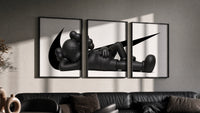 Reclining black KAWS Companion framed poster set of 3 with swoosh marks triptych in three black frames on a grey wall…