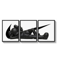Reclining black KAWS Companion framed poster set of 3 with swoosh marks three-panel set arranged as a triptych on a…