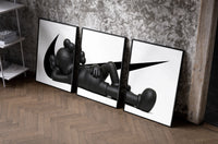 Reclining black KAWS Companion framed poster set of 3 with swoosh marks set of three black-framed prints leaning against…