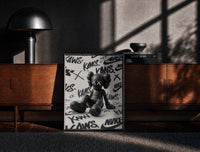Black-framed Sitting KAWS Companion framed poster print on a moody console with designer coffee-table books