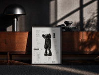 Black-framed KAWS Companion technical spec sheet framed poster on cream print on a moody console with designer…