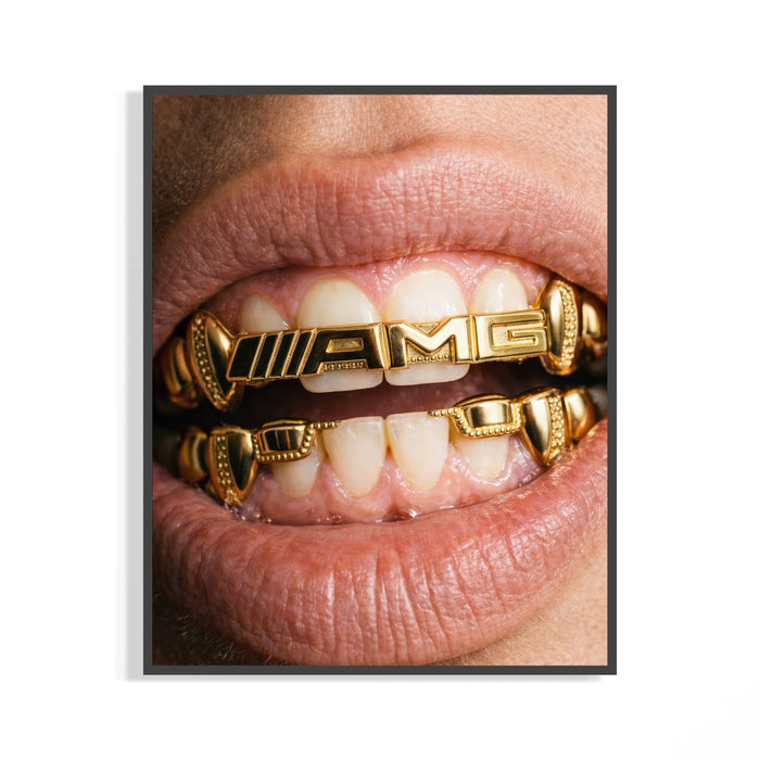 Macro close-up of gold AMG-branded grillz in a mouth shown in a dark frame on a white background